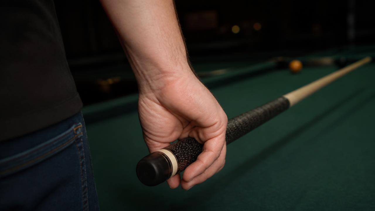 Close-up of a pool player's back hand cradling the wrapped butt of a cue with a relaxed neutral wrist